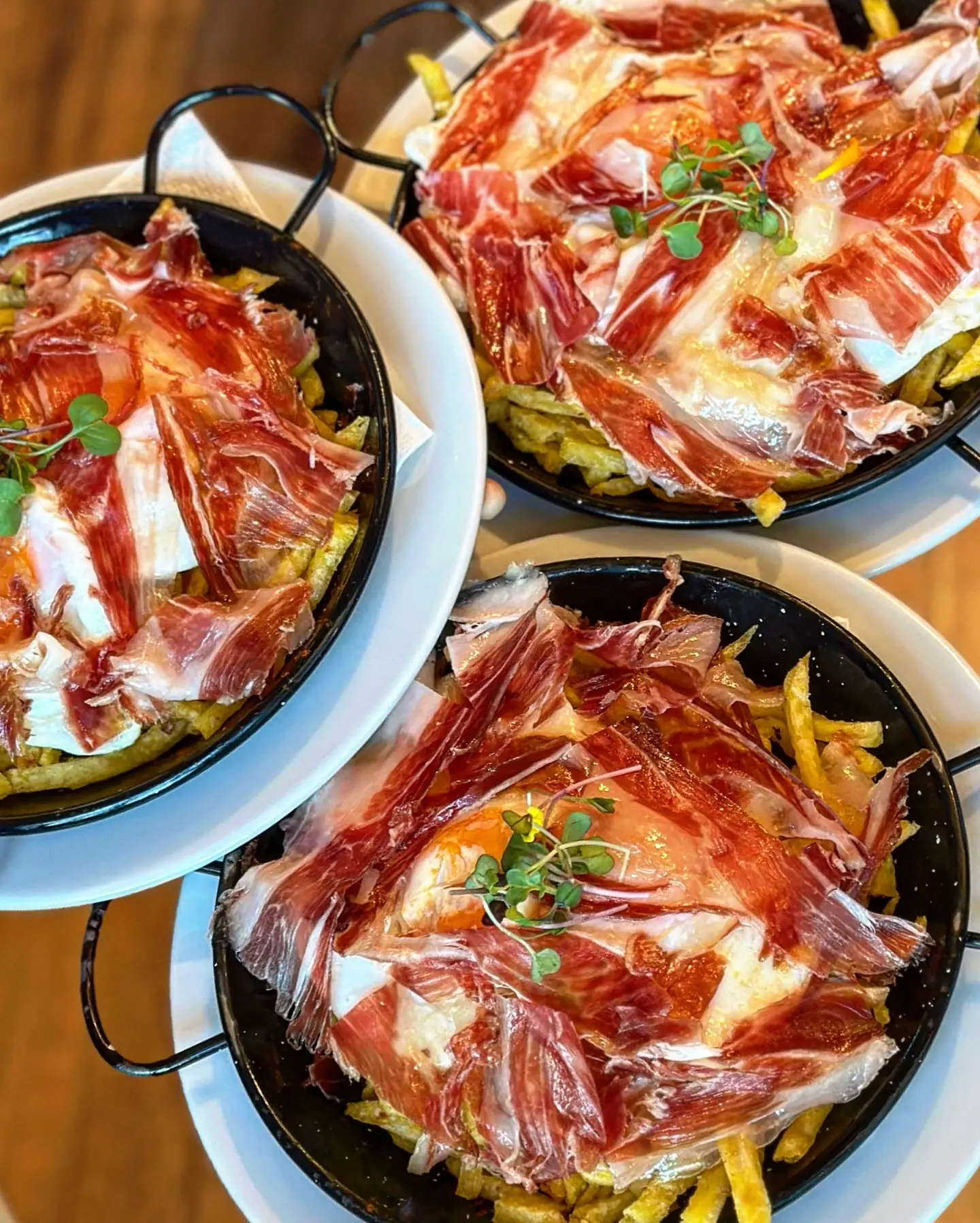 Pans of broken eggs over fries with cured ham