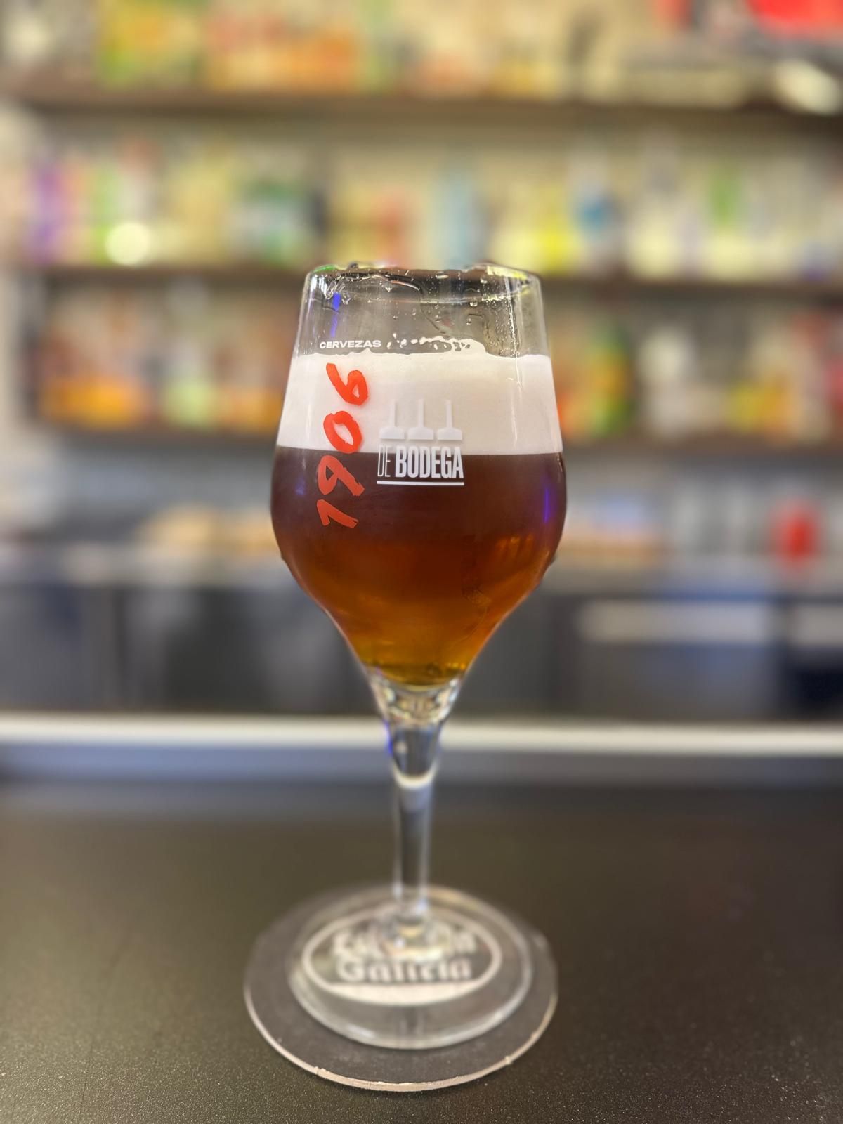 A glass of 1906 cellar beer with a full head of foam on the bar